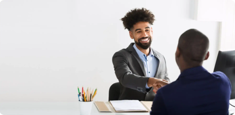 A smiling man shakes hands with someone sat across the table from them.