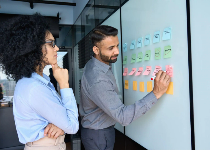 A man writing on a whiteboard with a woman watching.